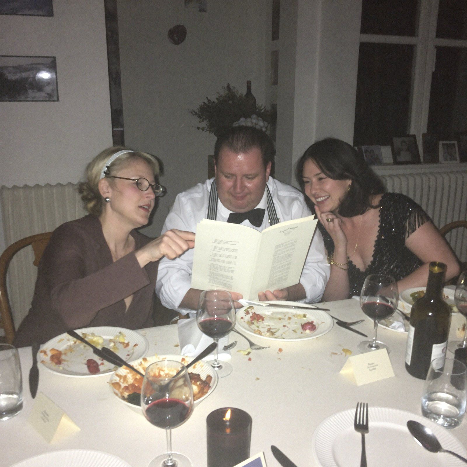 Three guests conferring over dinner, mid-investigation
